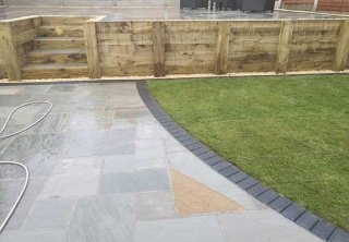 A full rear landscape involving retaining wall using sleepers, patio using a charcoal edging pavior, a kandla grey indian sanstone and grass area returfed at a job in Gedling, Nottingham A full rear landscape involving retaining wall using sleepers, patio using a charcoal edging pavior, a kandla grey indian sanstone and grass area returfed at a job in Gedling, Nottingham